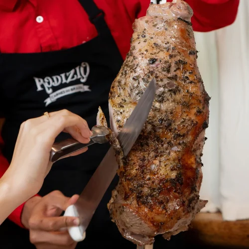 Mesero cortando rodizo de carne de pierna de cordero